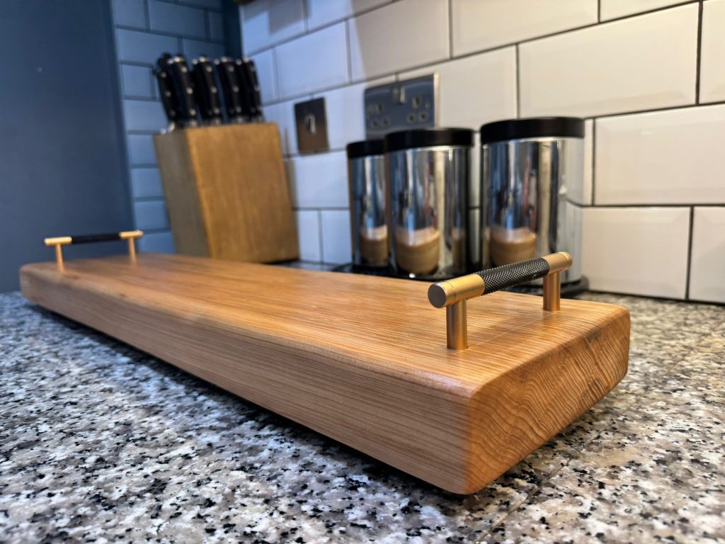 A wooden cutting board with a handle, showcasing a smooth surface and natural grain patterns.